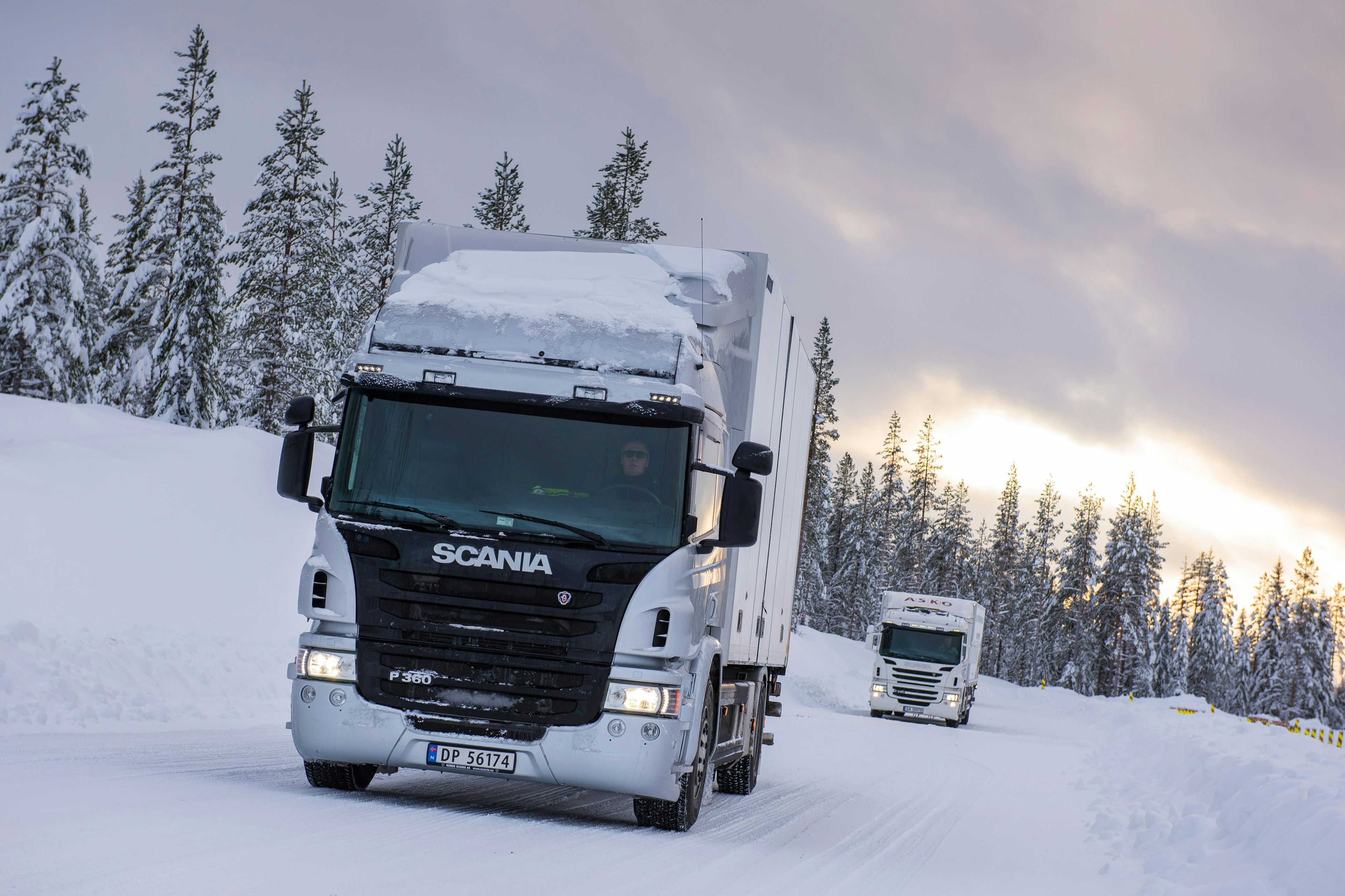Ett snölandskap med två lastbilar som kör på vägen