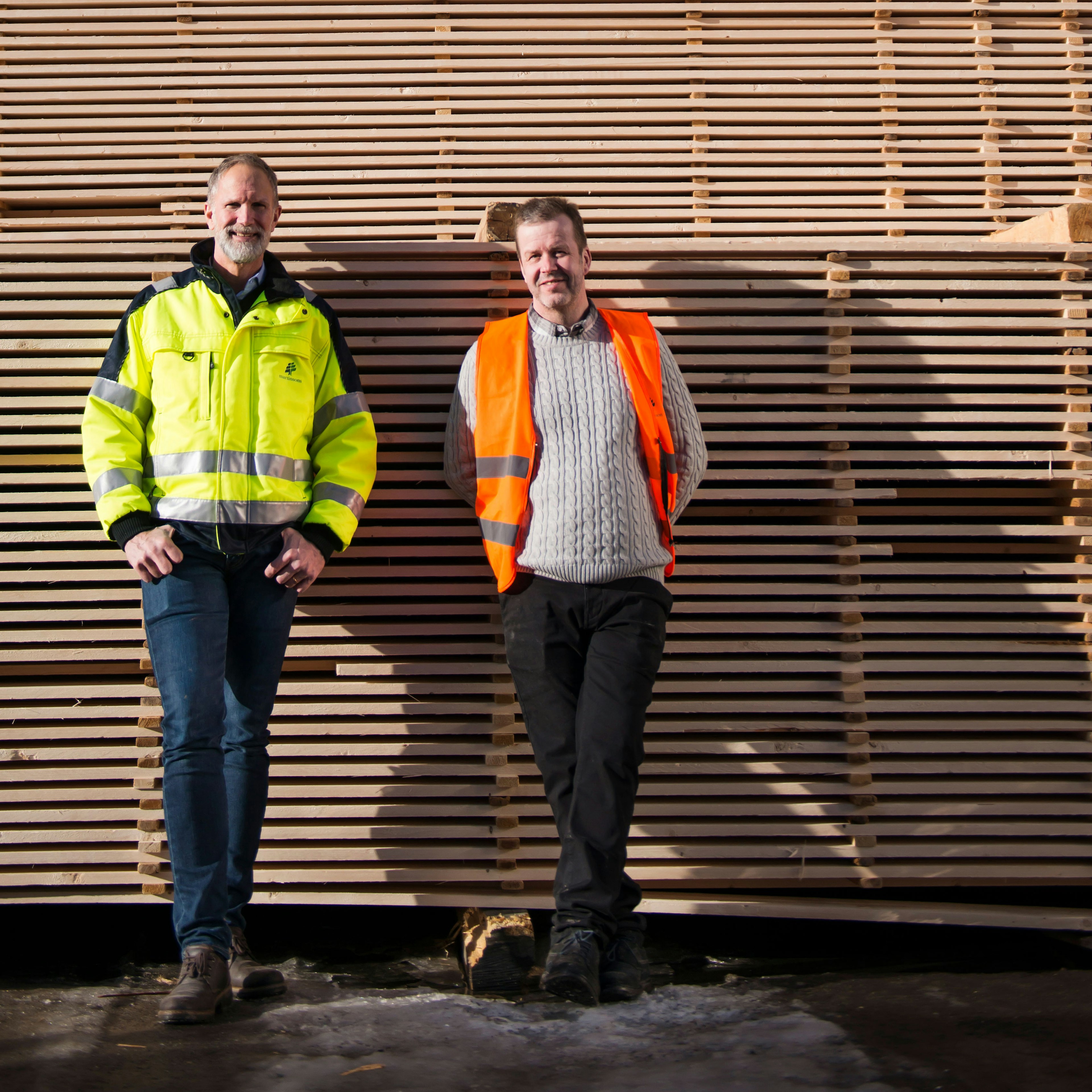 Två män i arbetskläder lutar sig mot en vägg utomhus