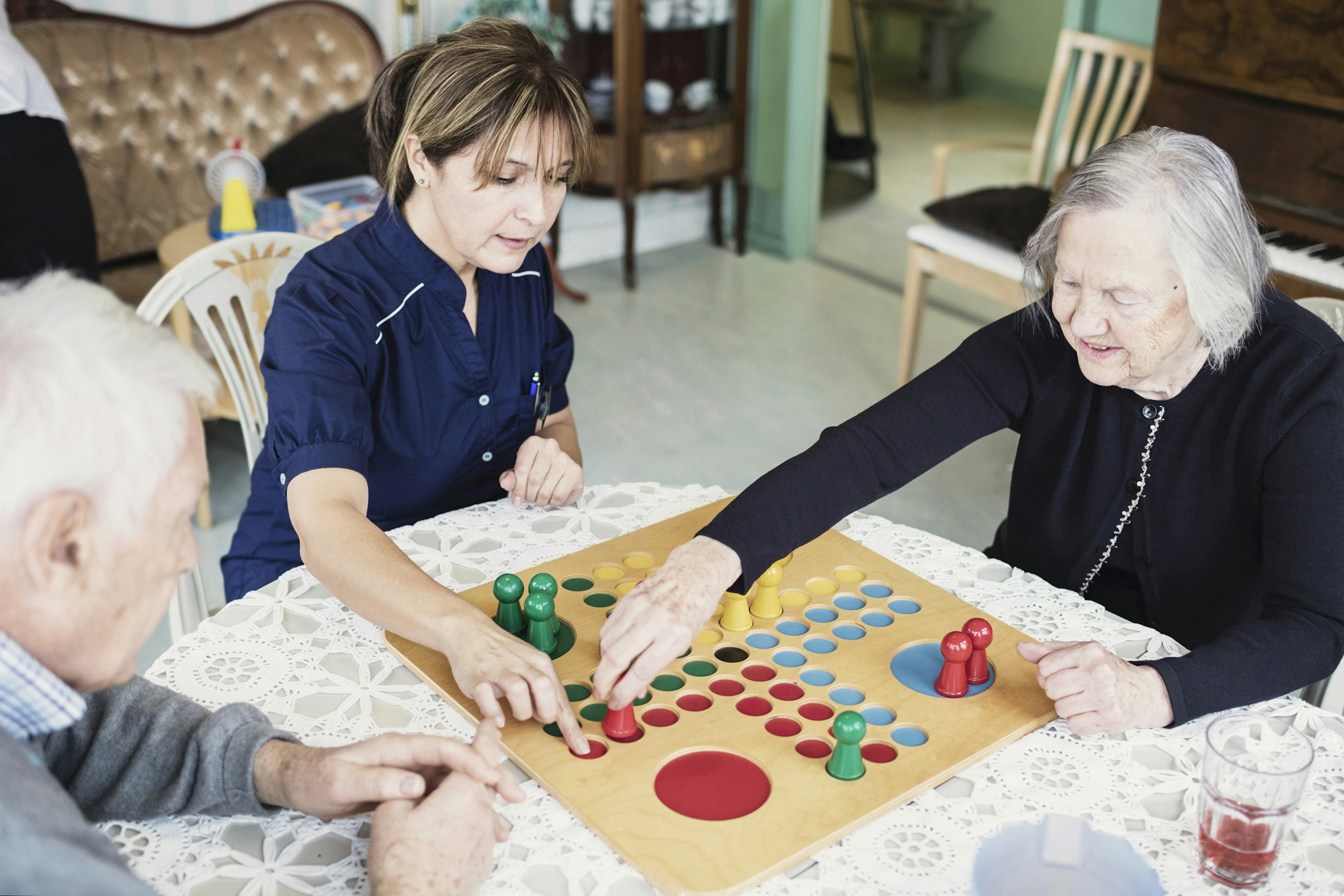 Vårdarbetare spelar spel med en äldre man och kvinna 