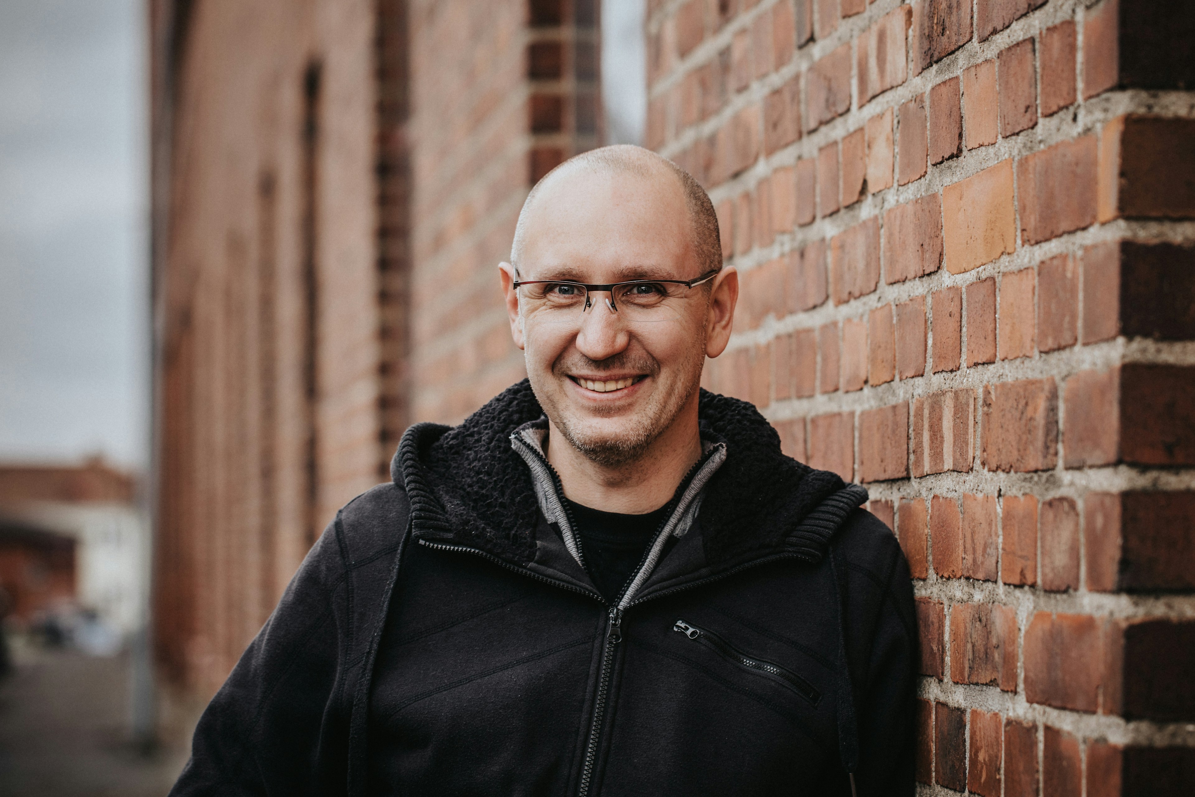 Porträtt på en man i glasögon som lutar sig mot en tegelvägg