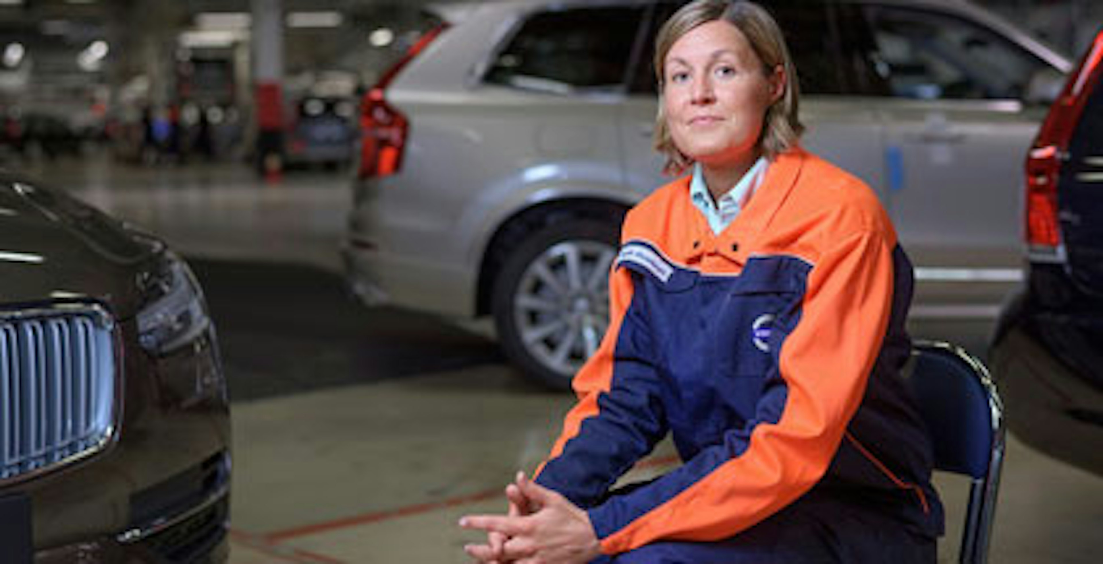 En kvinnlig anställd på Volvo sitter på en stol i en lokal med bilar